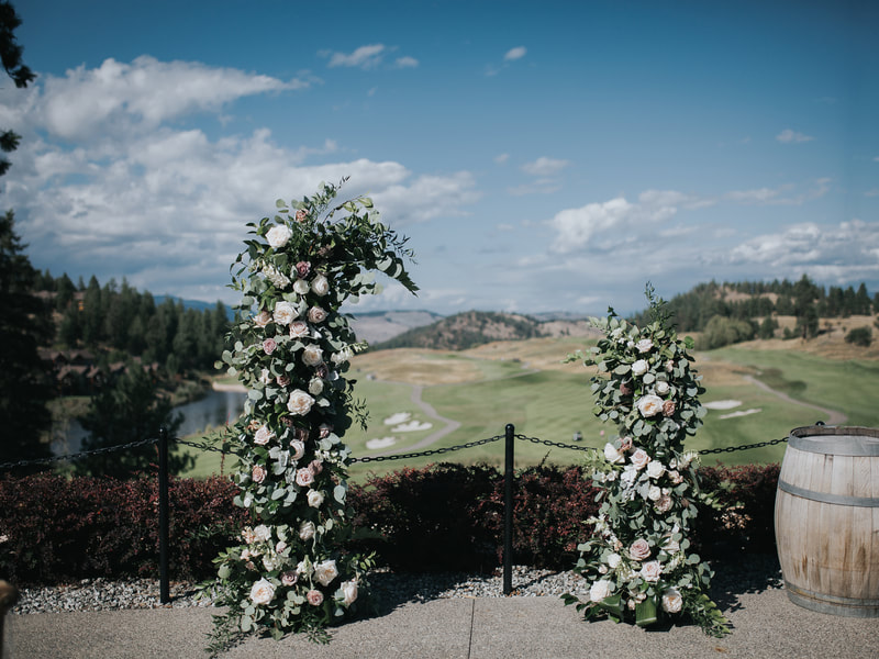 Wedding of Bride Samantha and Groom Andrew, ceremony at Predator Ridge in Kelowna, BC.  On a clear, bright day overlooking the golf course.  Floral installation backdrop pillars of pink, white roses and greenery towers.  Bride’s bouquet and groom’s boutonniere of matching roses, spray roses, dahalias and garden roses.  Wedding photos taken by Heatherly Photography.  Wedding flowers done by Sweet Elegance Floral design, florist in Kelowna, BC.  