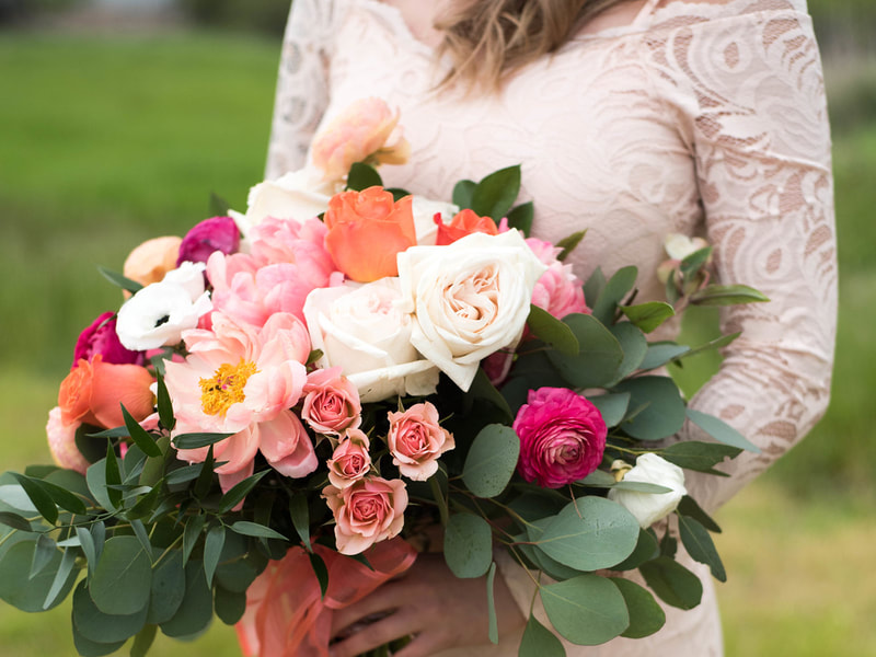 Bridal bouquet, bride’s bouquet with flowers done by Sweet Elegance Floral design florist in Kelowna, BC.
Hand tied summer bouquet with anemones, ranunculus, roses, garden roses, peonies, astilbe, and eucalyptus in pink, orange and yellow with flowing pink ribbons. 
